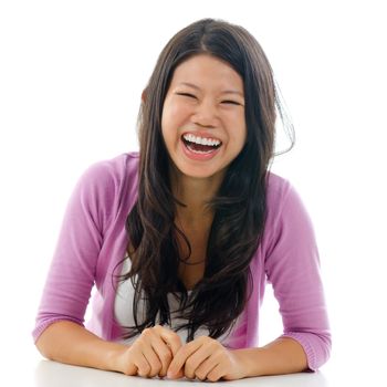 Candid portrait Asian woman laughing with mouth opened big. Sitting isolated on white background.