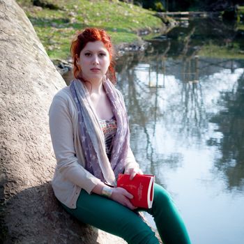 beautiful red head young woman reading book in the park