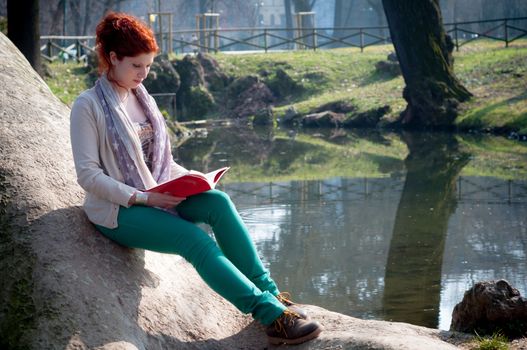 beautiful red head young woman reading book in the park