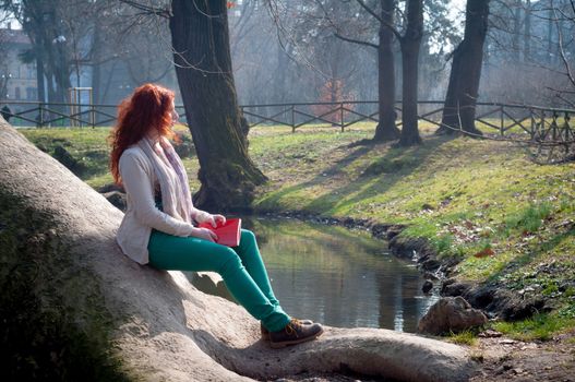 beautiful red head young woman reading book in the park