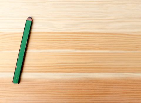 Green carpenter pencil on a wood background with copy space