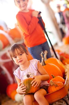 Cute Girl Riding A Wagon with Her Pumpkin and Sister At A Pumpkin Patch One Fall Day.