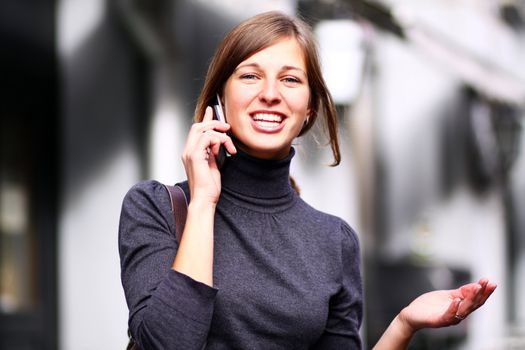 Young happy woman calling by phone on the street