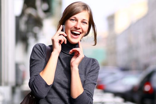 Young happy woman calling by phone on the street