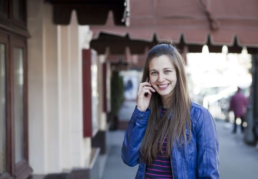 Young happy woman calling by phone on the street