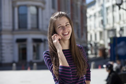 Young happy woman calling by phone on the street