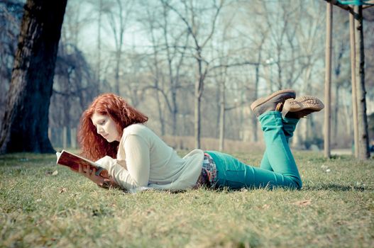 beautiful red head young woman reading book in the park