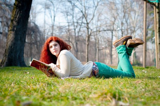 beautiful red head young woman reading book in the park