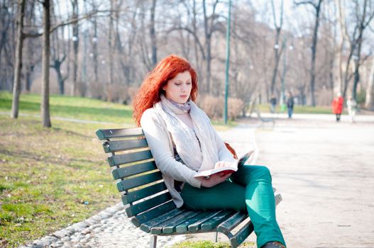 beautiful red head young woman reading book in the park