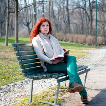 beautiful red head young woman reading book in the park