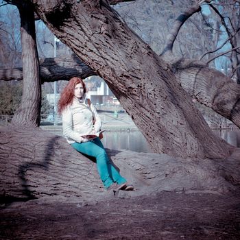 beautiful red head young woman reading book in the park