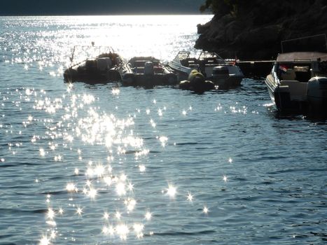 A beautiful sunny day on the crystal waters of the Adriatic Sea near Rovinj, Croatia. The sun is dazzling through romantic and peaceful reflexes on the quiet waves, while sleeping boats are resting on the background waiting for a fisher or a romantic couple taking a rest.