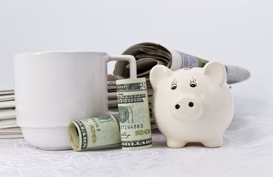 Iconic symbols of United States currency, white savings bank, newspapers, and coffee mug depict the American economy in the news.  