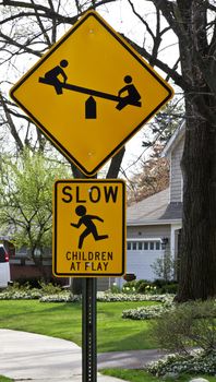 Children at Play road sign in neighborhood cautions to drive slowly; depicts children on see saw and running child.  Location is Northbrook, Illinois, a suburb of Chicago in the United States. 