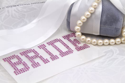 Wedding celebration image with BRIDE spelled in pink jewel letters, a gray velvet jewelry box, and white pearls, on damask with ribbon aross top image; copy space; 