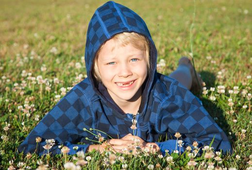 A cute happy smiling young boy with missing front teeth lying in grass with clover.