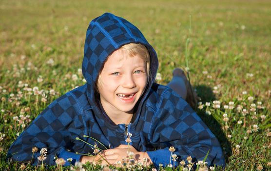 A cute happy smiling boy lying in grass with clover with missing front teeth.