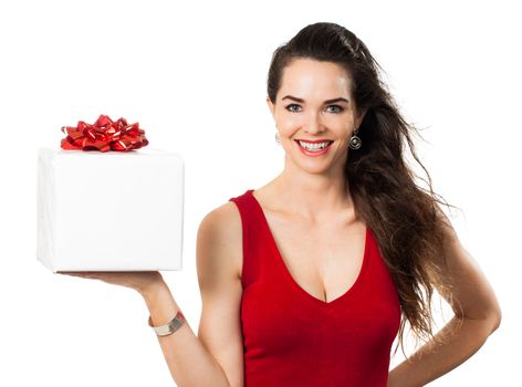 A happy woman in a red dress smiling and holding out a beautifully wrapped christmas gift. Isolated on white.