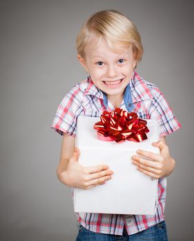 A very happy cute young boy holding a large gift or present and smiles at camera.