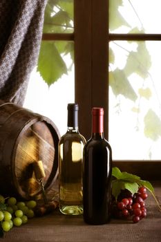 Wine bottles with grapes and barrel on old wooden table