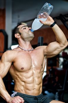 Muscular male bodybuilder in a gym drinking water or energy drink from bottle