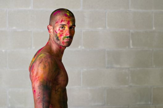 Handsome young man with skin painted all over with bright Holi colors