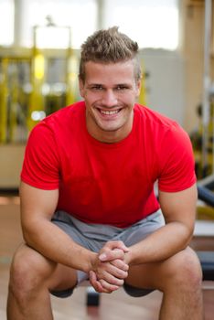 Handsome young man in gym sitting on bench, smiling and looking in camera