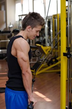 Teen bodybuilder working out with gym equipment, exercising triceps with cables