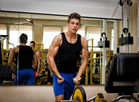 Teen bodybuilder working out with gym equipment, exercising pecs muscles with cables