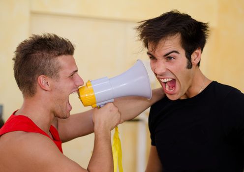 Personal trainer motivating male client by yelling against him with megaphone