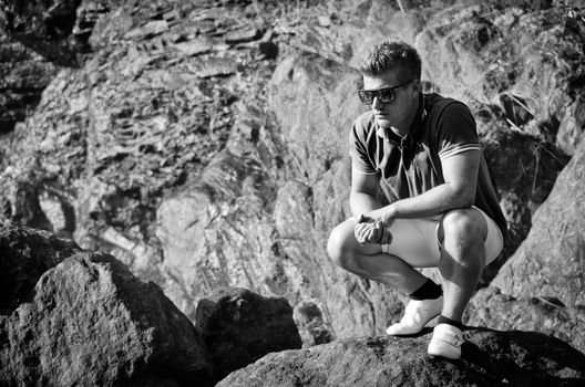 Handsome young man on stone looking down, black and white photo