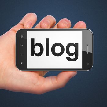 SEO web development concept: hand holding smartphone with word Blog on display. Generic mobile smart phone in hand on Dark Blue background.