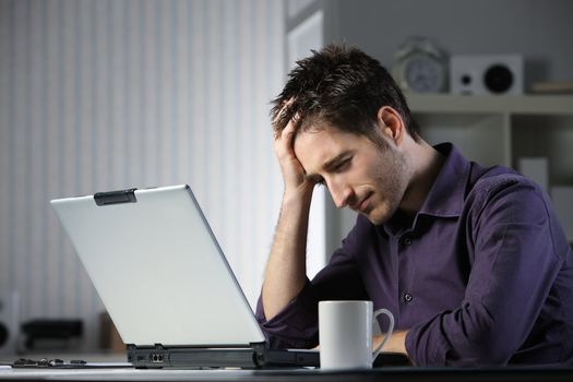 Unhappy stressed male student looking at his laptop computer with his head in his hands