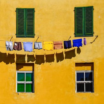 Detail of colorful yellow house walls, windows and drying clothes in square format