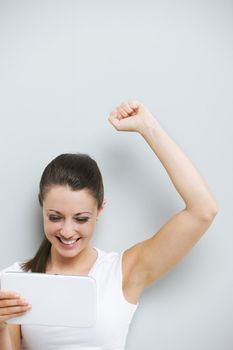 Pretty young woman with arm raised in the air looking her touchpad