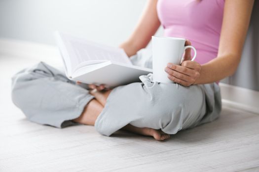 Close up of young woman with book and a cup of coffee sitting on floor