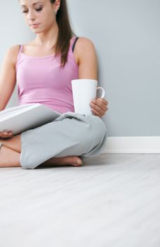Young woman with book and a cup of coffee sitting on floor, focus on hand