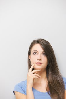 A lovely young brunette looking away thoughtfully against grey background