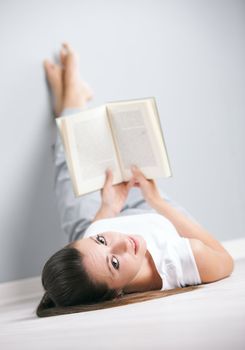 Portrait of a cute young female laying by the wall reading a book
