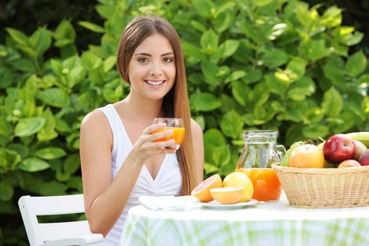 Young woman relaxes in the garden drinking a orange juice