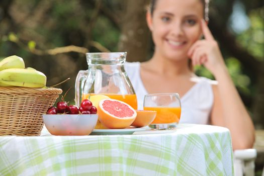 Table with fruit and orange juice, smiling woman on background