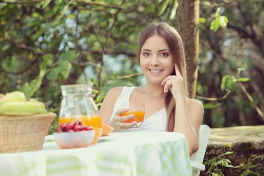 Young woman relaxes in the garden drinking a orange juice