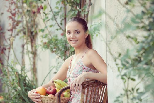 Beautiful girl with a basket of fresh fruit, sitting outdoors
