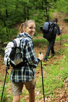 Young couple enjoying nordic walking in a forest, woman looking at camera