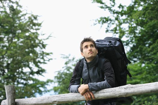 A young man with backpack resting on a wooden fence