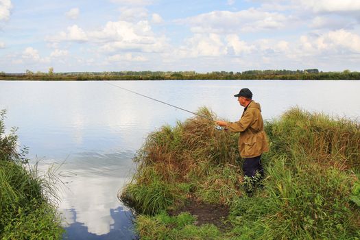 old fisherman with spinning rod on lake