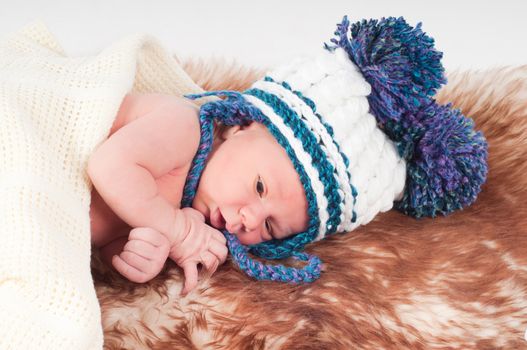 Shot of newborn baby in hat with pom-pom lying on fur