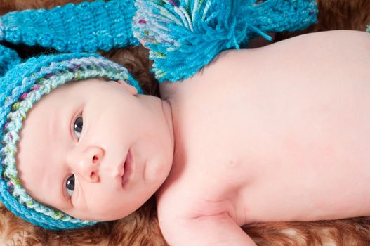 Shot of newborn baby in blue knitted hat lying on fur