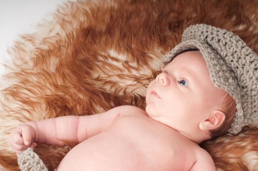 Shot of newborn baby in knitted hat lying on fur