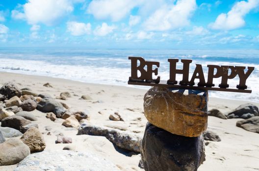 Sign "Be happy" on the top of rocks balancing by Pacific ocean 